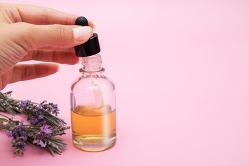 Obraz na płótnie Canvas Womans hand draws liquid into a pipette from a glass bottle on a pink background with lavender flowers, copy space