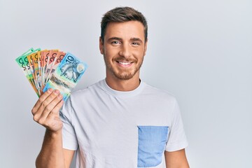 Handsome caucasian man holding australian dollars looking positive and happy standing and smiling with a confident smile showing teeth © Krakenimages.com