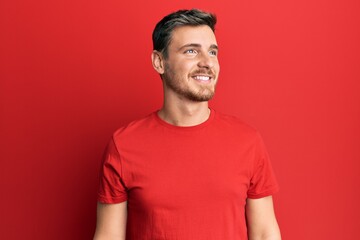Fototapeta premium Handsome caucasian man wearing casual red tshirt looking away to side with smile on face, natural expression. laughing confident.