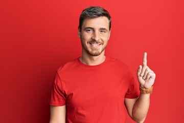 Handsome caucasian man wearing casual red tshirt pointing finger up with successful idea. exited and happy. number one.