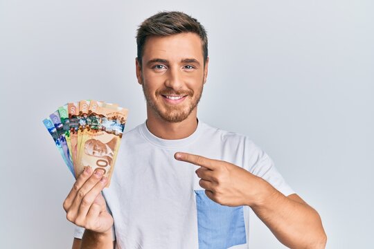 Handsome caucasian man holding canadian dollars smiling happy pointing with hand and finger
