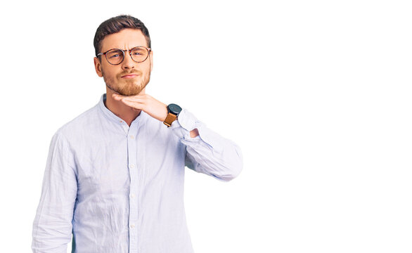Handsome young man with bear wearing elegant business shirt and glasses cutting throat with hand as knife, threaten aggression with furious violence