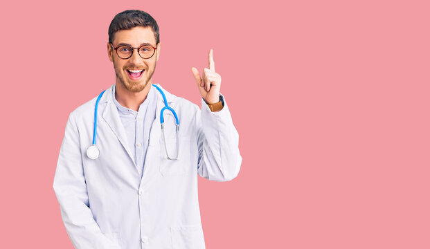 Handsome young man with bear wearing doctor uniform pointing finger up with successful idea. exited and happy. number one.