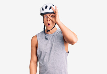 Young handsome man wearing bike helmet doing ok gesture shocked with surprised face, eye looking through fingers. unbelieving expression.