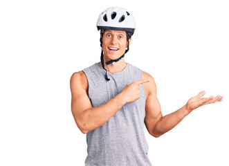 Young handsome man wearing bike helmet amazed and smiling to the camera while presenting with hand and pointing with finger.