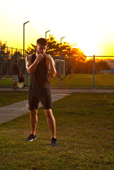 Athlete trains on a sunset background. The boxer warms up near the stadium. Contrasting dramatic shadows on the face as an artistic effect. The guy on the playground.