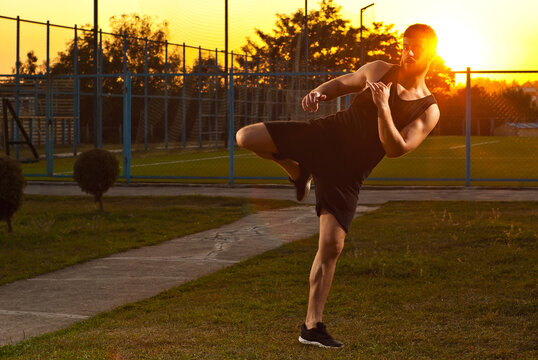 Athlete trains on a sunset background. The boxer warms up near the stadium. Contrasting dramatic shadows on the face as an artistic effect. The guy on the playground.