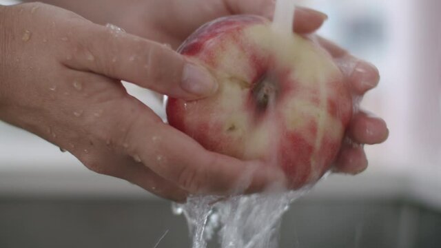 Close-up shot of washing flat peach under the water jet before eating