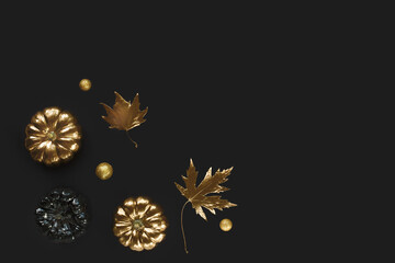 Obraz premium Trendy background with black and gold flying Halloween pumpkin, maple leaves on isolated on black background. Flat lay, top view, copy space.