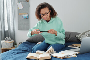 Young mixed-race contemporary student photographing pages with text