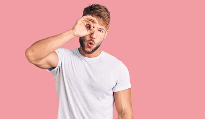 Young caucasian man wearing casual white tshirt doing ok gesture shocked with surprised face, eye looking through fingers. unbelieving expression.