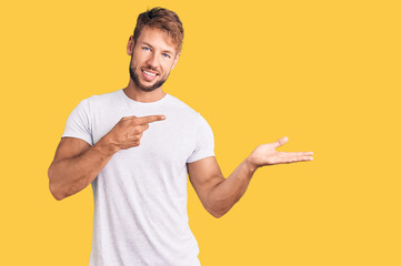 Young caucasian man wearing casual white tshirt amazed and smiling to the camera while presenting with hand and pointing with finger.