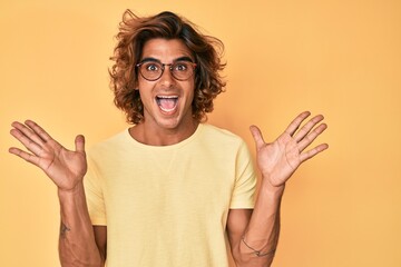 Young hispanic man wearing casual clothes and glasses celebrating victory with happy smile and winner expression with raised hands