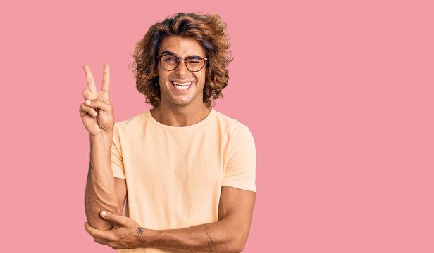 Young hispanic man wearing casual clothes and glasses smiling with happy face winking at the camera doing victory sign. number two.