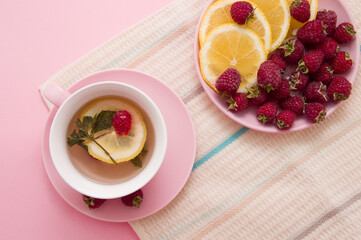 lemon wedges and raspberries in a pink plate, a cup of tea on a pink background. Flat lay of summer. Food concept