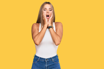 Fototapeta premium Young blonde woman wearing casual style with sleeveless shirt afraid and shocked, surprise and amazed expression with hands on face