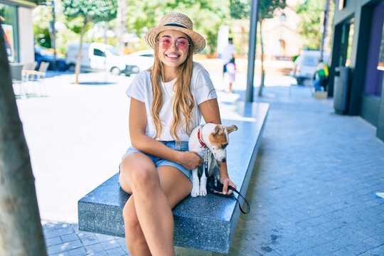 Young beautiful blonde woman walking the dog outside on a summer day sitting on a bench