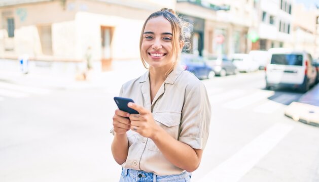 Young beautiful blonde caucasian woman smiling happy outdoors on a sunny day using smartphone