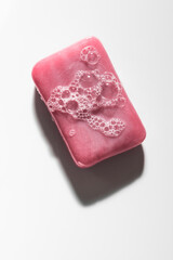 Classic pink bar of soap with bubbles shot in strong light against a white surface.