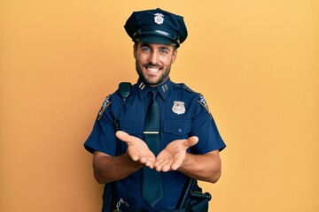 Obraz premium Handsome hispanic man wearing police uniform smiling with hands palms together receiving or giving gesture. hold and protection
