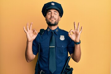 Handsome hispanic man wearing police uniform relaxed and smiling with eyes closed doing meditation gesture with fingers. yoga concept.