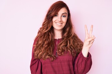 Young beautiful woman wearing casual winter sweater smiling with happy face winking at the camera doing victory sign. number two.