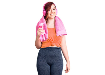 Young beautiful woman wearing sportswear and headphones holding bottle of water looking positive and happy standing and smiling with a confident smile showing teeth