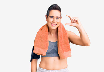 Fototapeta na wymiar Young woman with short hair wearing sportswear and towel using smartphone smiling and confident gesturing with hand doing small size sign with fingers looking and the camera. measure concept.