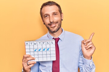 Young handsome man holding travel calendar smiling happy pointing with hand and finger to the side