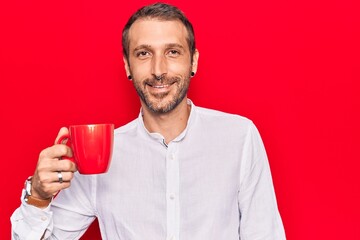 Young handsome man holding coffee looking positive and happy standing and smiling with a confident smile showing teeth