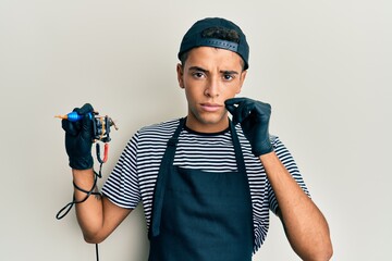 Young handsome african american man tattoo artist wearing professional uniform and gloves holding...
