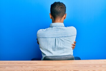 Fototapeta premium Young handsome african american man wearing casual clothes sitting on the table standing backwards looking away with crossed arms