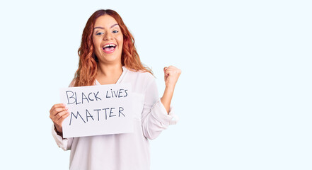 Young latin woman holding black lives matter banner screaming proud, celebrating victory and...