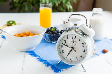 Time for breakfast. Alarm clock with healthy food on the background. Bowl with cereals, nuts and...