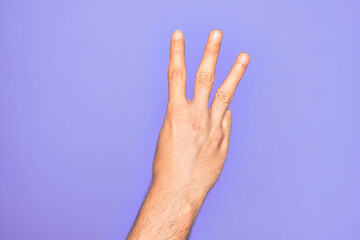 Hand of caucasian young man showing fingers over isolated purple background counting number 3 showing three fingers