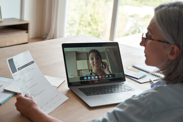 Old female hr reading cv during online job interview by video call. Senior employer checking indian seeker resume talking by social distance remote recruitment chat meeting videoconference on laptop. - obrazy, fototapety, plakaty