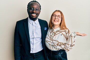 Young interracial couple wearing business and elegant clothes smiling cheerful presenting and pointing with palm of hand looking at the camera.