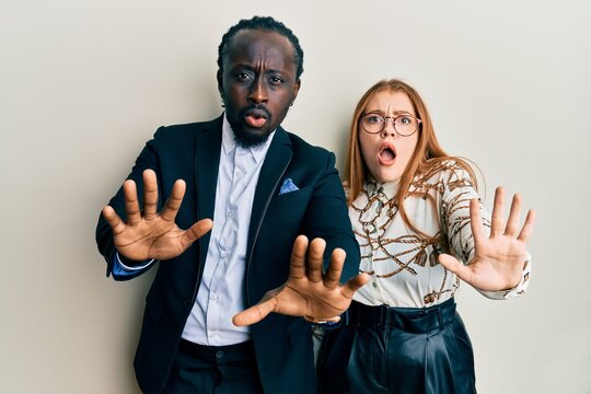Young interracial couple wearing business and elegant clothes doing stop gesture with hands palms, angry and frustration expression