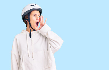 Beautiful brunette young woman wearing bike helmet and sporty clothes shouting and screaming loud to side with hand on mouth. communication concept.