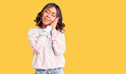 Young beautiful mixed race woman wearing casual tie dye sweatshirt sleeping tired dreaming and posing with hands together while smiling with closed eyes.