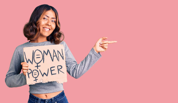 Young beautiful mixed race woman holding woman power banner smiling happy pointing with hand and finger to the side