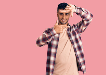 Obraz premium Young hispanic man wearing casual clothes smiling making frame with hands and fingers with happy face. creativity and photography concept.
