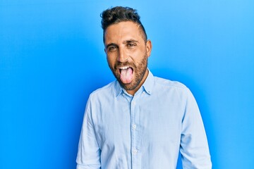 Handsome man with beard wearing casual clothes sticking tongue out happy with funny expression. emotion concept.