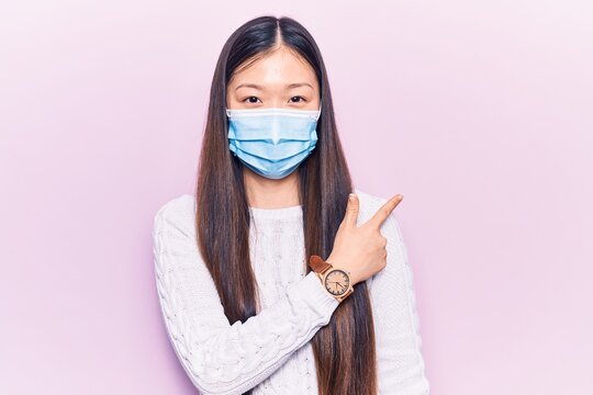 Young Beautiful Chinese Woman Wearing Medical Mask Smiling Cheerful Pointing With Hand And Finger Up To The Side