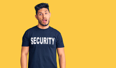 Handsome latin american young man wearing security t shirt in shock face, looking skeptical and sarcastic, surprised with open mouth