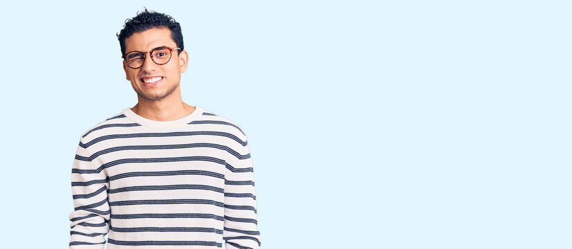 Hispanic handsome young man wearing casual clothes and glasses winking looking at the camera with sexy expression, cheerful and happy face.