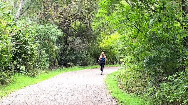 Rear view of a women running on a dirt trail in the woods wearing black spandex on her legs.