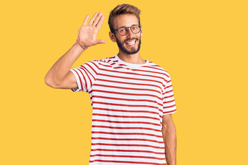 Fototapeta premium Handsome blond man with beard wearing casual clothes and glasses waiving saying hello happy and smiling, friendly welcome gesture