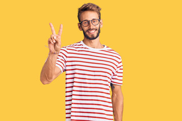 Handsome blond man with beard wearing casual clothes and glasses smiling looking to the camera...