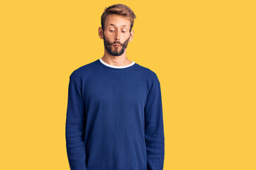 Handsome blond man with beard wearing casual sweater making fish face with lips, crazy and comical gesture. funny expression.